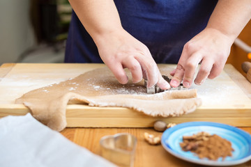 Female hands cutting a cookie with a cookie cutter. Dough is placed on the wooden board, on the wooden kitchen table