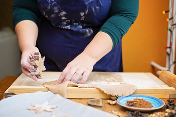 Young caucasian woman standing behind a table, baking for christmas. She is holding cookie cutter with a raw cookie in the shape of star.