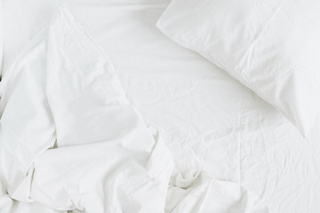 Flat lay of white bed with pillows, blanket and sheet. Top view minimal linen concept.