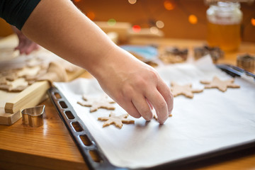 Close up photo of female hand placing a raw cookie in a shape of star on the baking pan lined with a white baking paper. Christmas baking concept.