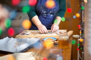 Young woman baking ginger bread at home, christmas lights at the foreground.