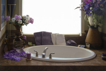 Romantic Bathtub and Fixtures Interior.  A romantic and beautifully decorated deep tub in a contemporary home with candles, books, towels and flowers lit with window light.