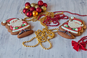 Cute Santa figures made of glazed honey cookies laying near red bow knot, golden beads and decorative balls on light wooden background