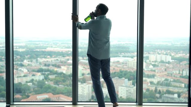 Drunk man drinking beer by window at home
