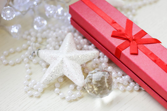 Red gift box, glittery white star, crystal ball and perly white beads on a white wooden background