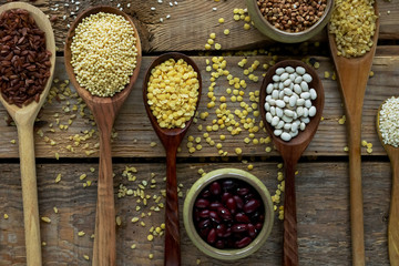 Raw organic cereal grains, seeds and beans in wooden spoons on rustic wooden background