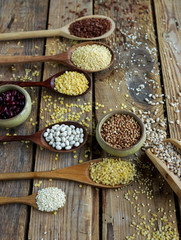 Raw organic cereal grains, seeds and beans in wooden spoons on rustic wooden background