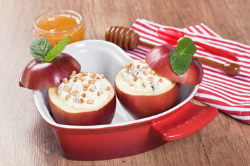 Baked apple desert / Baked apple stuffed cream cheese, raisins, fried almond slices, honey, mint in red casserole dish in form heart on wooden background
