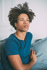 Portrait of a young thoughtful mixed race man sitting in the sofa