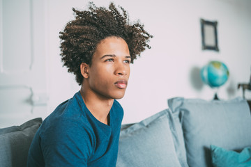 Portrait of a young thoughtful mixed race man sitting in the sofa