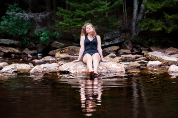 Young woman enjoying nature on peaceful, calm Red Creek river in Dolly Sods, West Virginia during sunny day with reflection dipping feet in water
