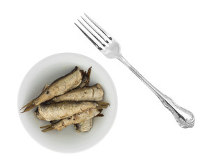Top view of canned smoked sprats in a small bowl with a fork to the side isolated on a white background.