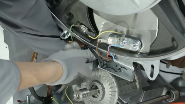 Experienced maintenance man carefully unscrewing another very long screw to release special part of washing machine.