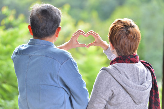 Portrait Of Happy Romantic Senior Couple Making Heart Shape With Hands Outdoor At The Green Nature Background