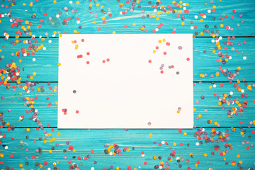 Colorful confetti and white paper on a wooden turquoise background .  Free copy space