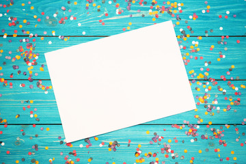 Colorful confetti and white paper on a wooden turquoise background .  Free copy space