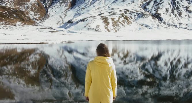 Back view of young female hiker enjoying the view of a peaceful mountain lake, French Alps, Sixt-Passy nature preserve, Lac d’Anterne.  4K UHD 60 FPS SLO MO