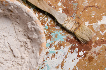 a brush next a bowl with dried putty on a hardboard