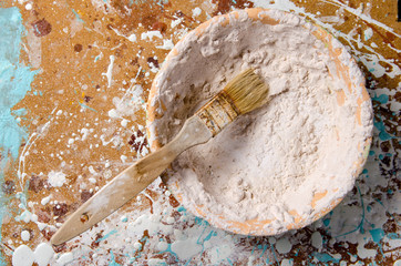 a brush into a bowl with dried putty on a hardboard