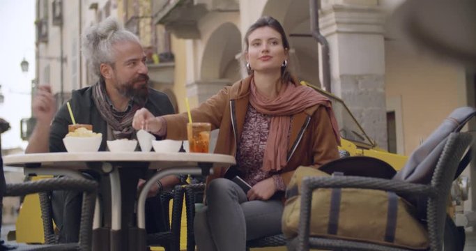 Woman and man talking having cocktail aperitif outside of cafe.Medium shot. Caucasian couple in love roadtrip vacation italian travel on convertible vintage car