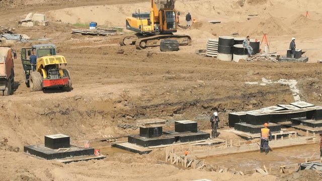 Large construction site. Workers in helmets and suits level surface and pour the foundation for building into wooden formwork outdoors
