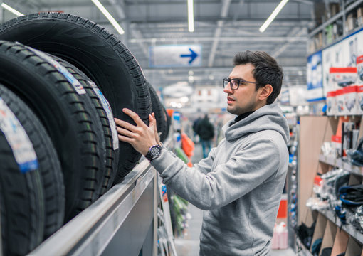 Smart customer taking new tires in the supermarket for buying. He looks happy. Big shopping mall with car goods.