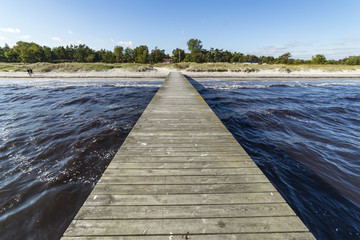A long wooden pier leading towards a sandy beach.  - obrazy, fototapety, plakaty