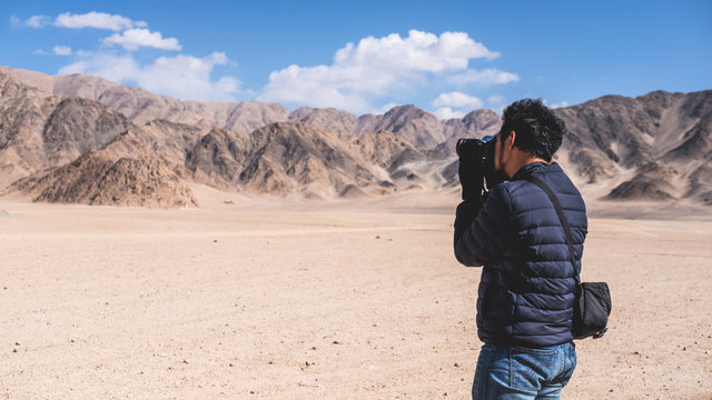A man photographer taking a landscape photo of desert , mountains and blue sky