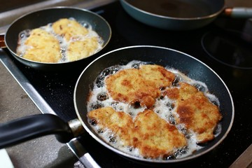 Traditional preparation of homemade Czech food - frying pan with oil and fried schnitzel coated...
