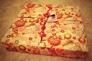Retro style picture of square present wrapped in yellow and red paper with red ribbon and decorations