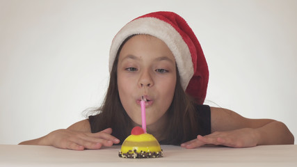 Beautiful naughty girl teenager in a Santa Claus hat blows out a candle on a festive cake on white background