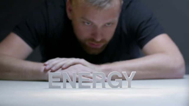 Young man looking on word energy composed from white letters on gray background