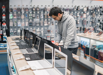Smart modern male customer choosing laptop in the computer store. difficult decision