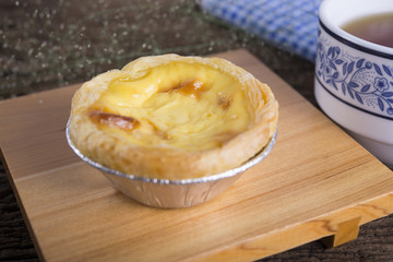egg tart on wooden plate with a cup of tea on the table