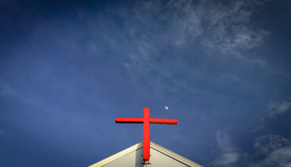 Red cross on the church with small moon, blue sky background.