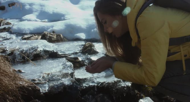 Young woman drinking water from outdoor mountain stream with her hands. 4K UHD SLO MO