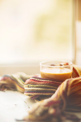 small and big red mug wrapped in a blue scarf and standing on the table against the background of a winter window / warming atmosphere for hanging out