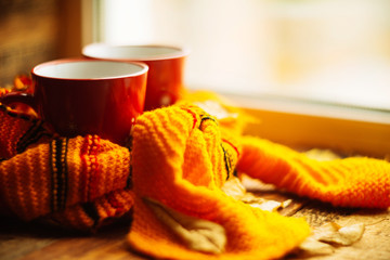 two red cups, wrapped in a scarf book and yellow leaves, autumn background, concept on the subject of comfort, warmth, pleasure, image toning