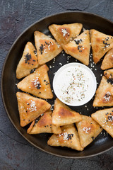 Top view of a metal tray with meat samosas and sauce, vertical shot, close-up