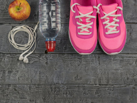 Beautiful pink sneakers, headphones, water and apples on a wooden floor. View from above.