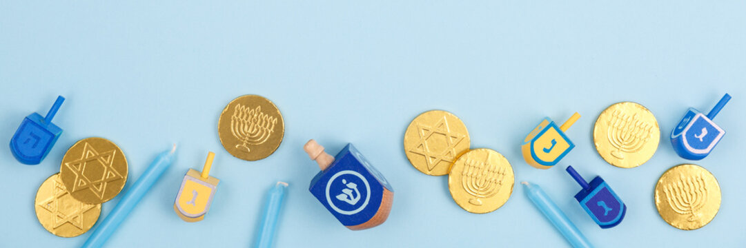 Blue background with multicolor dreidels, menora candles and chocolate coins. Hanukkah and judaic holiday concept.