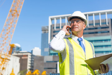 Man architector outdoor at construction area having mobile conversation