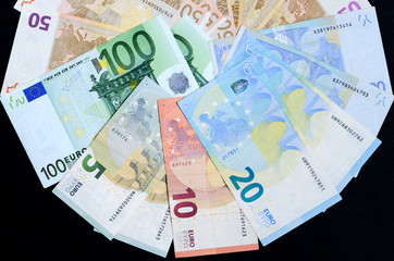 Euro banknotes of different values are laid out in a semicircle on the black background.