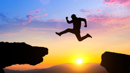 Man jumping over cliff on sunset background