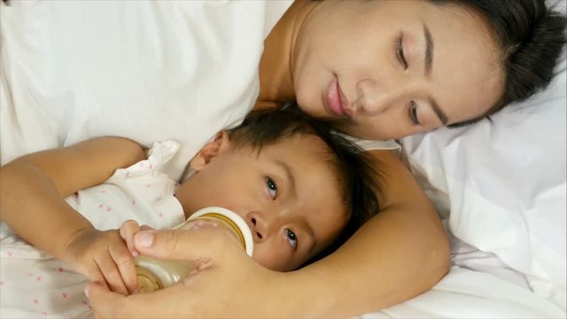 4k of young mother feeding baby a bottle in white bed