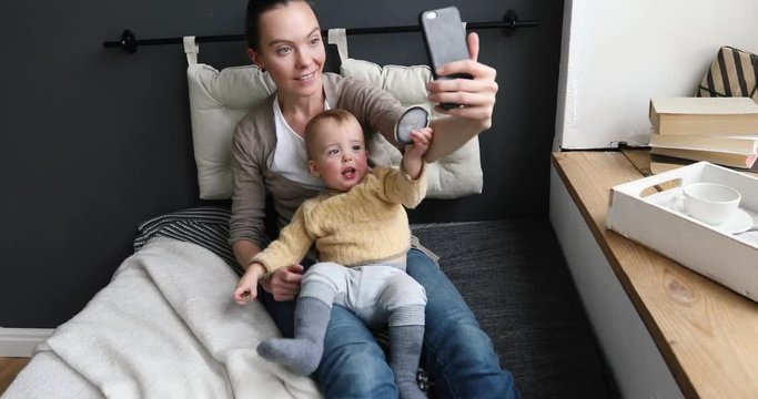 Mom and toddler taking selfie in cosy living room sitting on a sofa in front of a dark wall in the interior