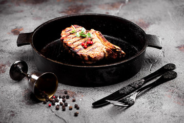 Grilled beef steak in a cast-iron frying pan on a concrete background