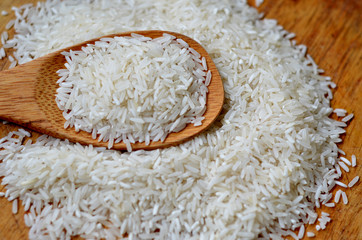 Heap of Jasmine Raw rice in wooden spoon on wooden table surface. Top view with selective focus