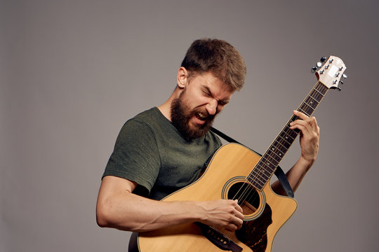 Man with a beard on a black background playing the guitar, emotions, musical instruments