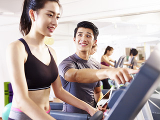 Fototapeta premium young asian adults exercising on treadmill helped by male trainer